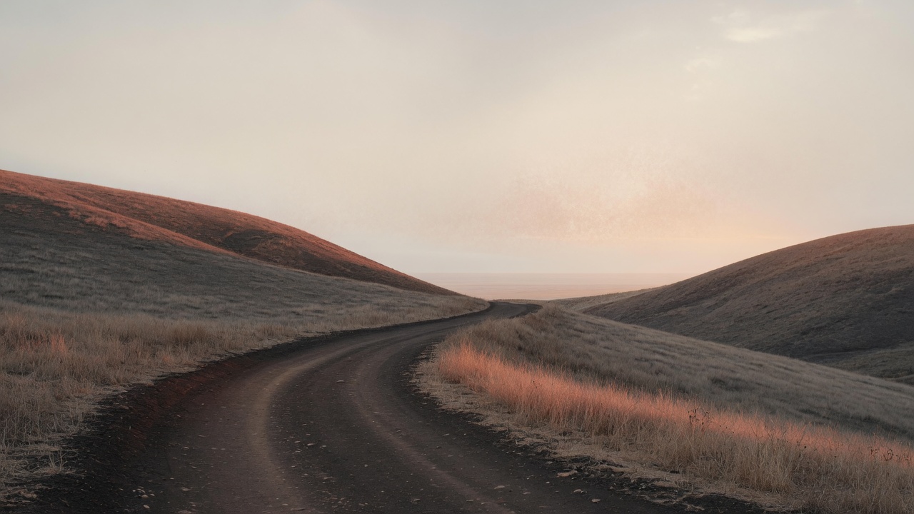 Una strada di terra che si apre tra colline, luce terracotta sul campo.